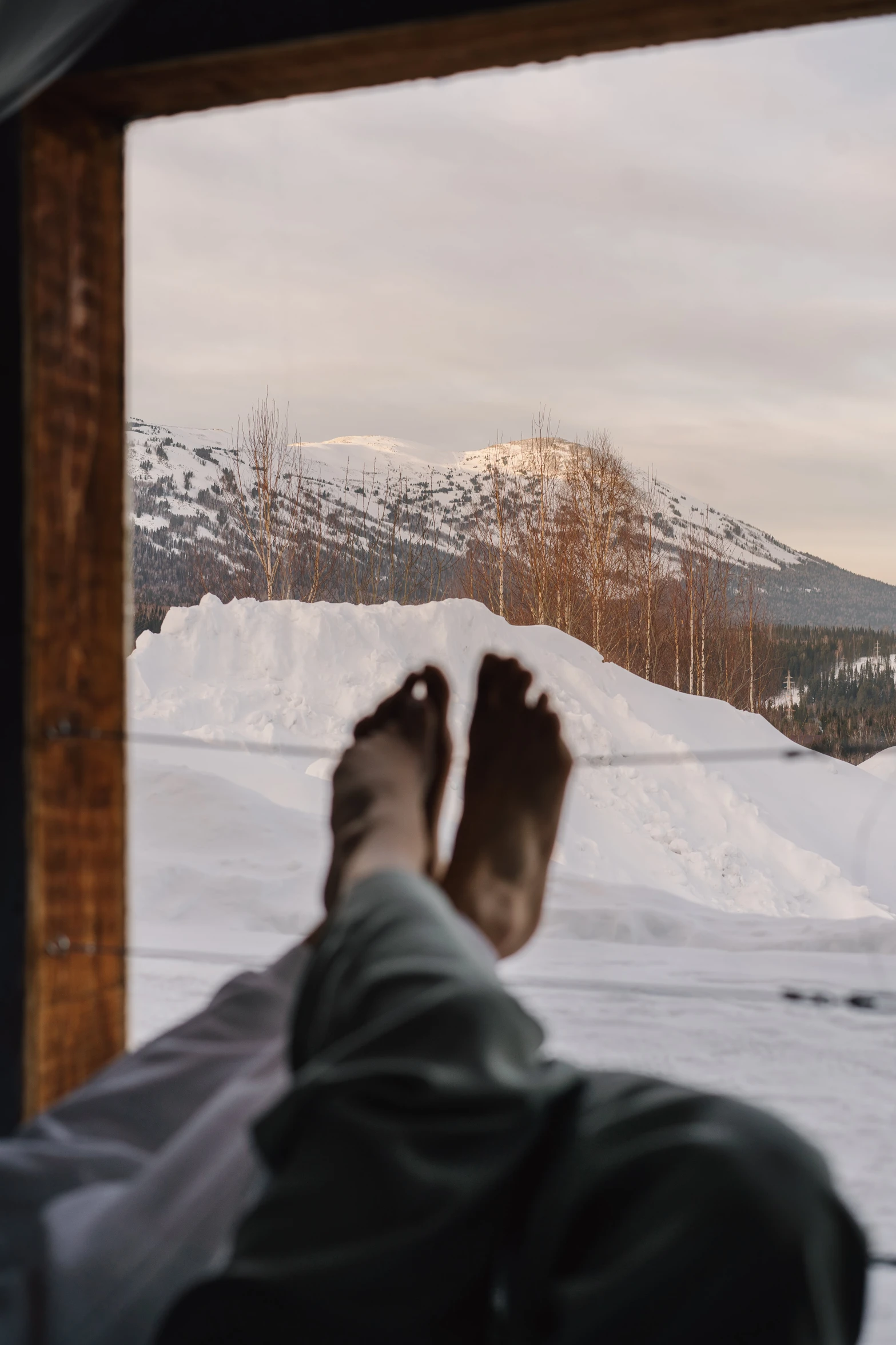 a person's feet sticking out of a window in the snow, some mountains in the background, relaxing, nordic, reclining