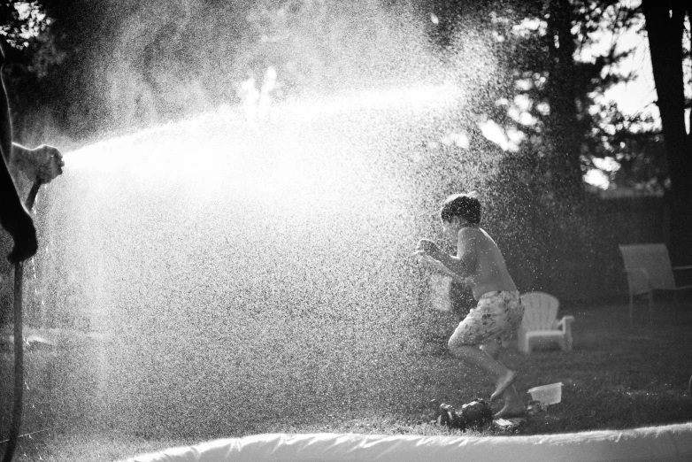 a black and white photo of a young boy playing in a sprinkler, by Felix-Kelly, slip n slide, lowres, gardening, summer light