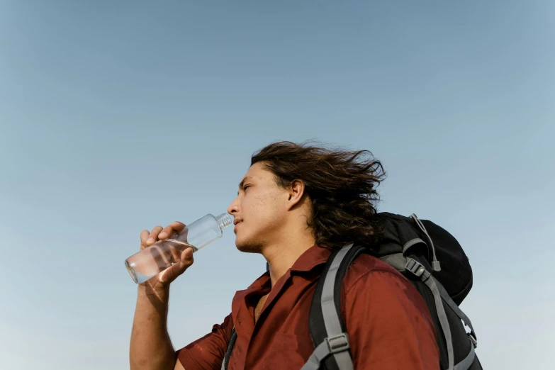 a man with a backpack is drinking water, pexels contest winner, avatar image, lean man with light tan skin, australian, clear sky