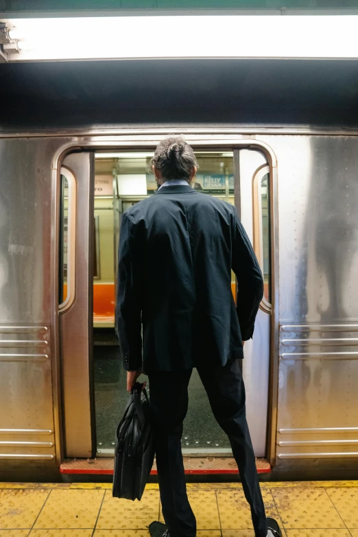 a man that is standing in front of a train, unsplash, renaissance, mta subway entrance, exiting from a wardrobe, back facing the camera, wearing a worn out suit