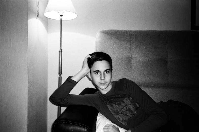 a black and white photo of a man sitting on a couch, inspired by Jean Malouel, portrait of 14 years old boy, with pointy ears, épaule devant pose, posing for a picture