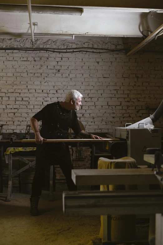 a man working on a piece of wood in a workshop, by Attila Meszlenyi, stillframe, architect, old man, full body image