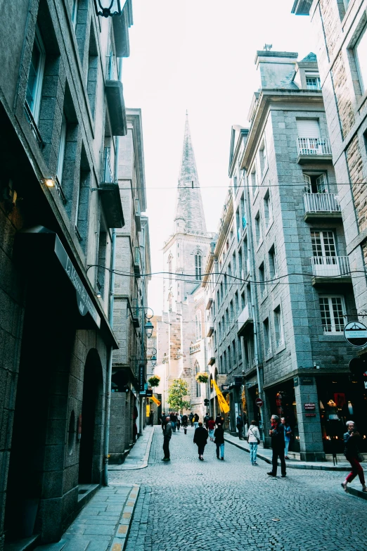 a group of people walking down a street next to tall buildings, a picture, renaissance, liege, tall stone spires, savannah, instagram post