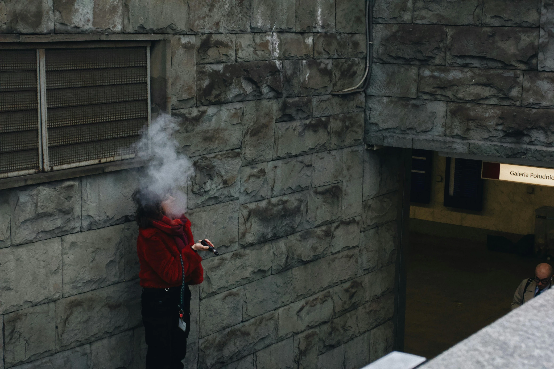 a person standing next to a wall smoking a cigarette, misting, a high angle shot, red mist, high walls