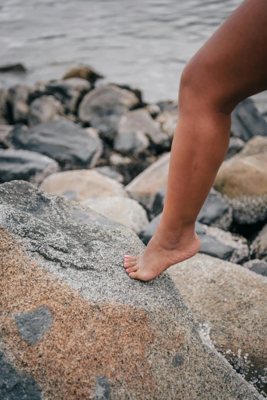 a woman standing on top of a rock next to a body of water, very close up foot shot, walking boy, slightly tanned, crawling