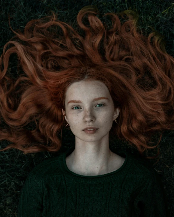 a woman laying on top of a lush green field, inspired by Elsa Bleda, unsplash contest winner, pre-raphaelitism, with long wavy red hair, on a gray background, portrait of anya taylor-joy, in front of a black background