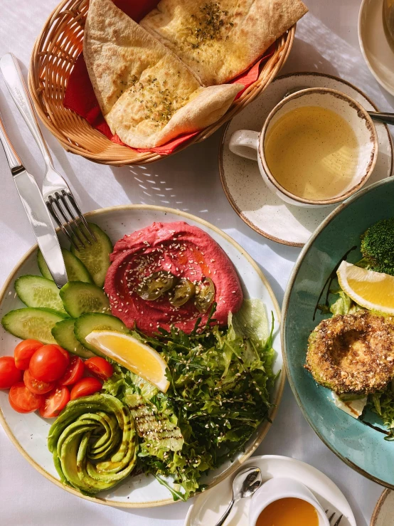 a table topped with plates of food next to cups of coffee, dau-al-set, salad, half image, humus, pink