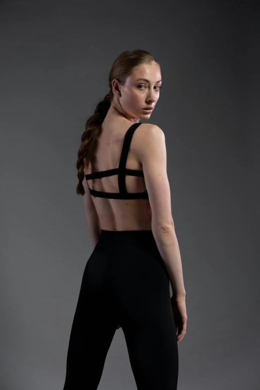 a woman in a black sports bra top and leggings, inspired by Elizabeth Polunin, facing away from camera, structure : kyle lambert, avant designer uniform, award - winning details