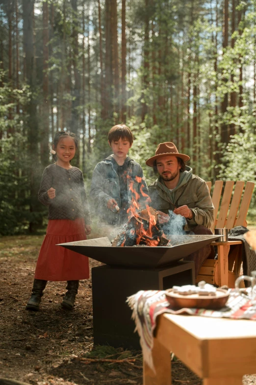 a group of people standing around a fire pit, alejandro inarritu, forest picnic, little kid, cooking