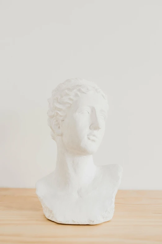 a white bust sitting on top of a wooden table, trending on unsplash, detailed product image, plaster, on a white table, hera