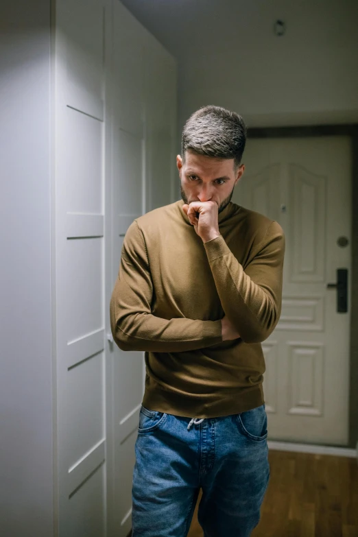a man standing in a hallway with his hand on his chin, brown sweater, ptsd, disappointed, jakub rebelka