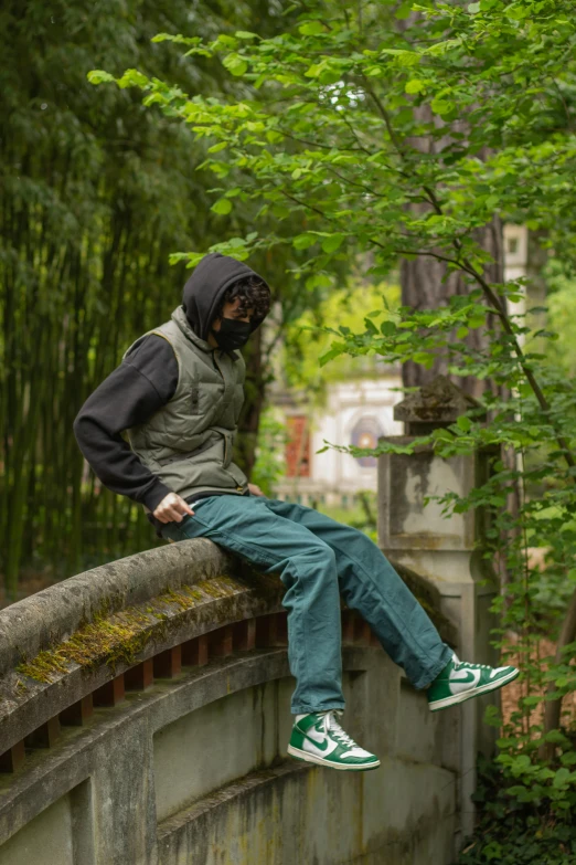 a man sitting on top of a stone bridge, an album cover, inspired by Ma Quan, unsplash, renaissance, green hood, cargo pants, balaclava, in japanese garden