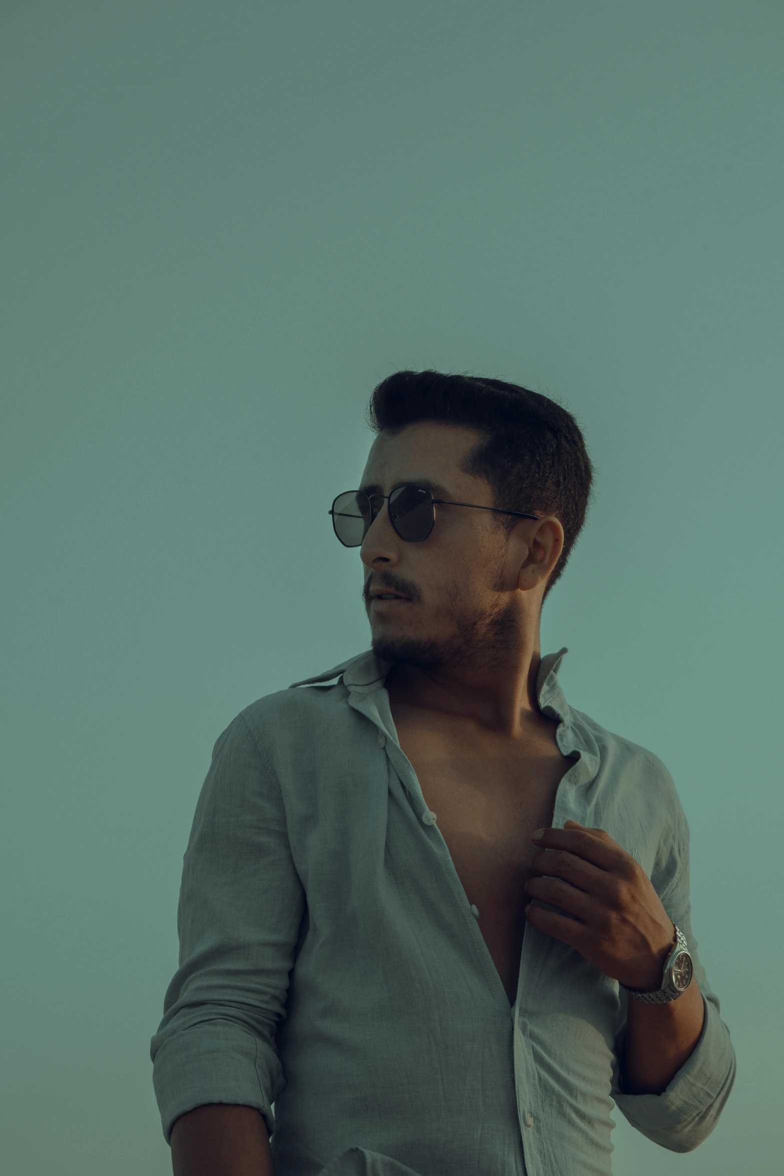 a man standing on top of a beach next to the ocean, an album cover, inspired by Camilo Egas, pexels contest winner, wearing shades, faded glow, handsome man, androgynous person