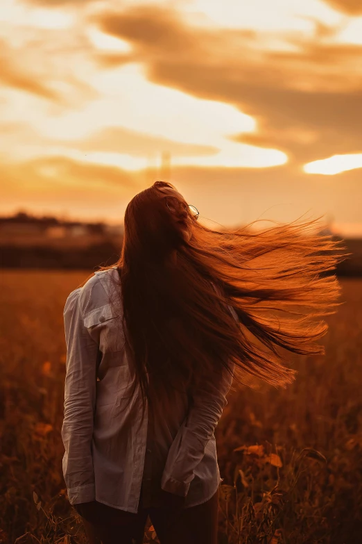 a woman standing in a field with her hair blowing in the wind, pexels contest winner, renaissance, ((sunset)), brown colored long hair, shot from a distance, fall season