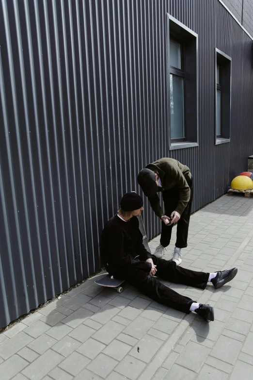 two men sitting on the ground in front of a building, a picture, unsplash, realism, skateboarder style, plain background, face down, low quality photo