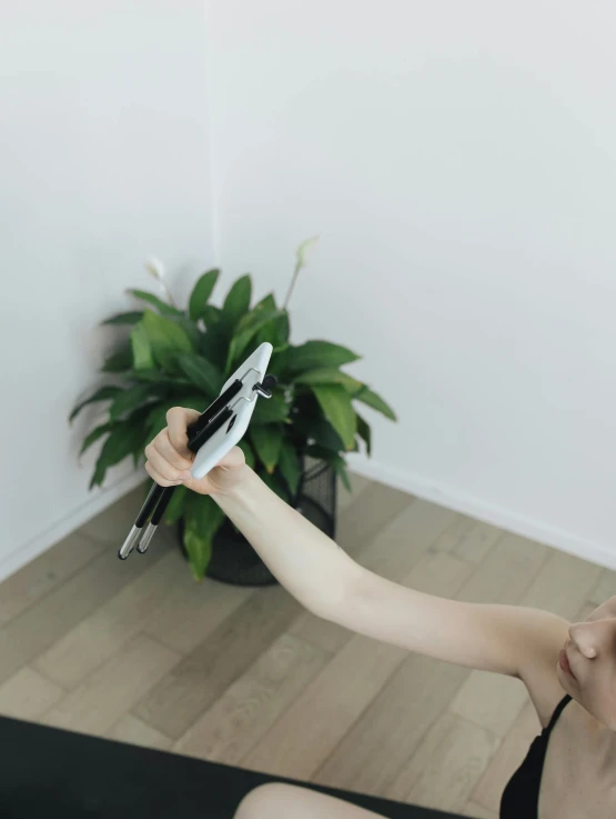 a woman sitting on the floor with a pair of scissors in her hand, unsplash, happening, holding a ray gun, next to a plant, yoga pose, low quality photo