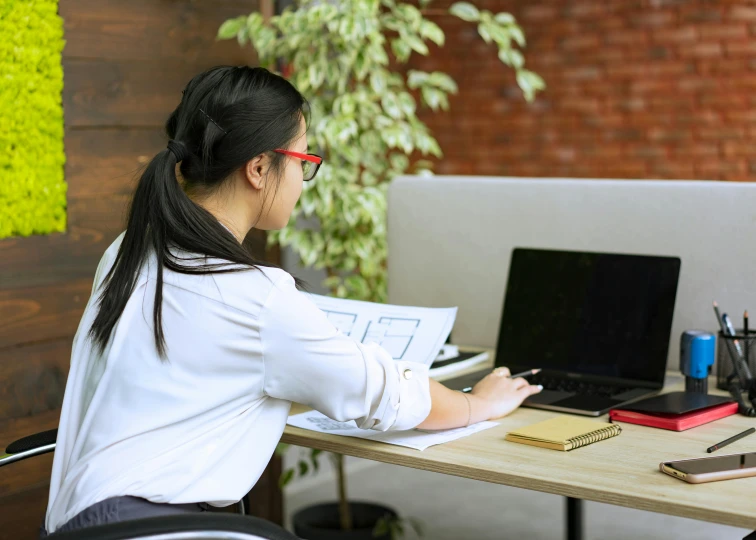 a woman sitting at a desk working on a laptop, by Nicolette Macnamara, pexels contest winner, profile image, asian female, bent - over posture, centre image