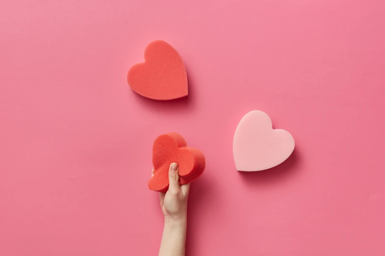 a woman's hand holding a paper heart on a pink background, an album cover, inspired by Valentine Hugo, trending on pexels, carved soap, various sizes, coral red, 3 colours