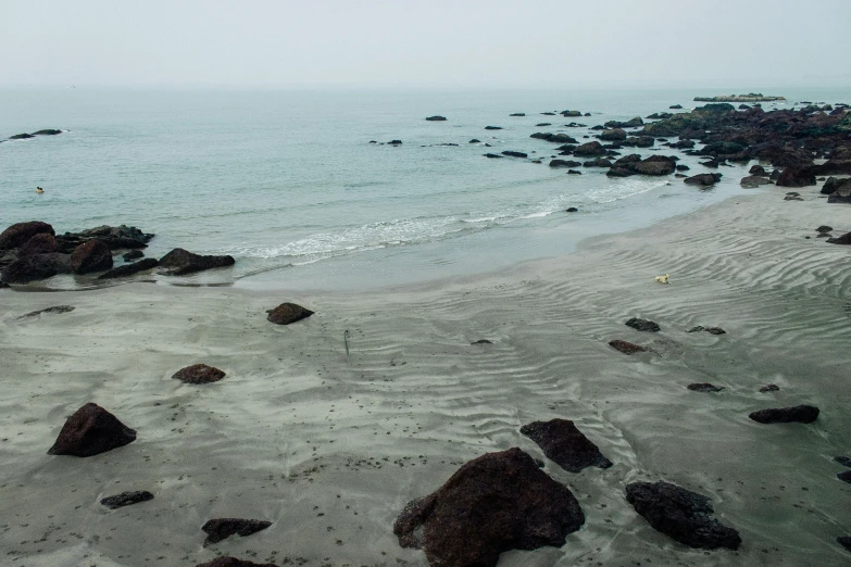 a person flying a kite on top of a sandy beach, pexels contest winner, minimalism, wet rocks, india, boulders, hazy water