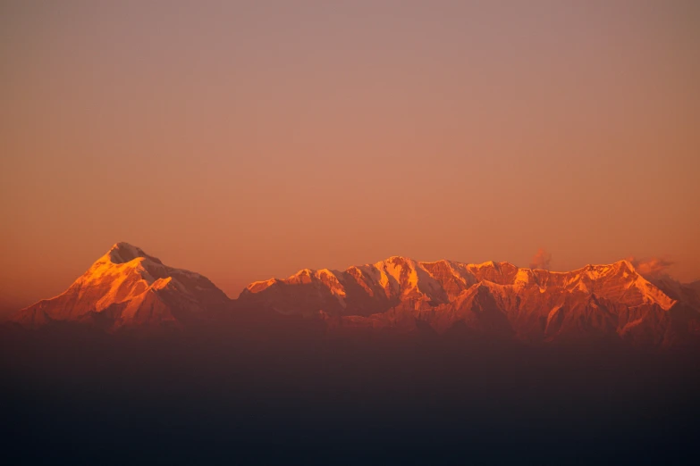 a plane flying over a mountain range at sunset, by Peter Churcher, pexels contest winner, romanticism, nepal, faded red colors, panorama, distant mountains lights photo