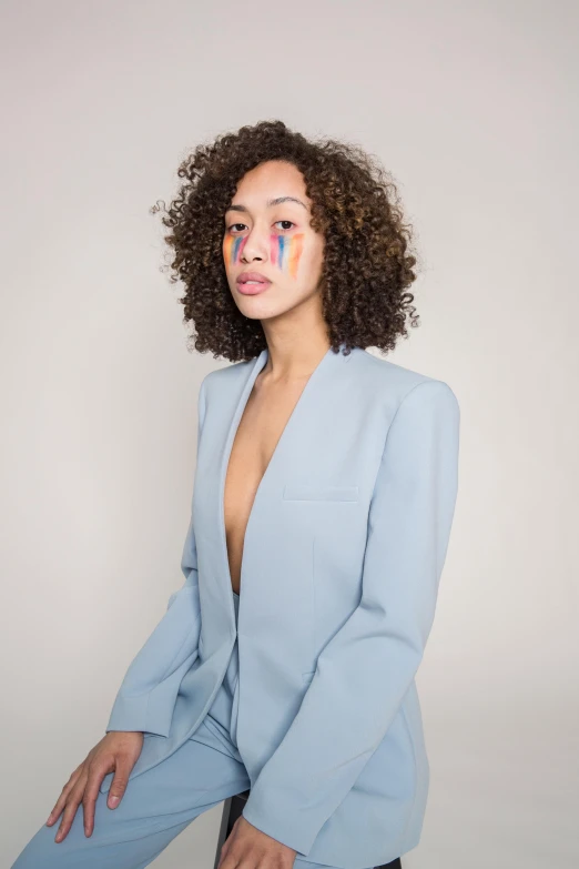 a woman in a blue suit sitting on a stool, an album cover, inspired by Louis Le Nain, trending on pexels, curly hair, pastel clothing, subject detail: wearing a suit, bella poarch