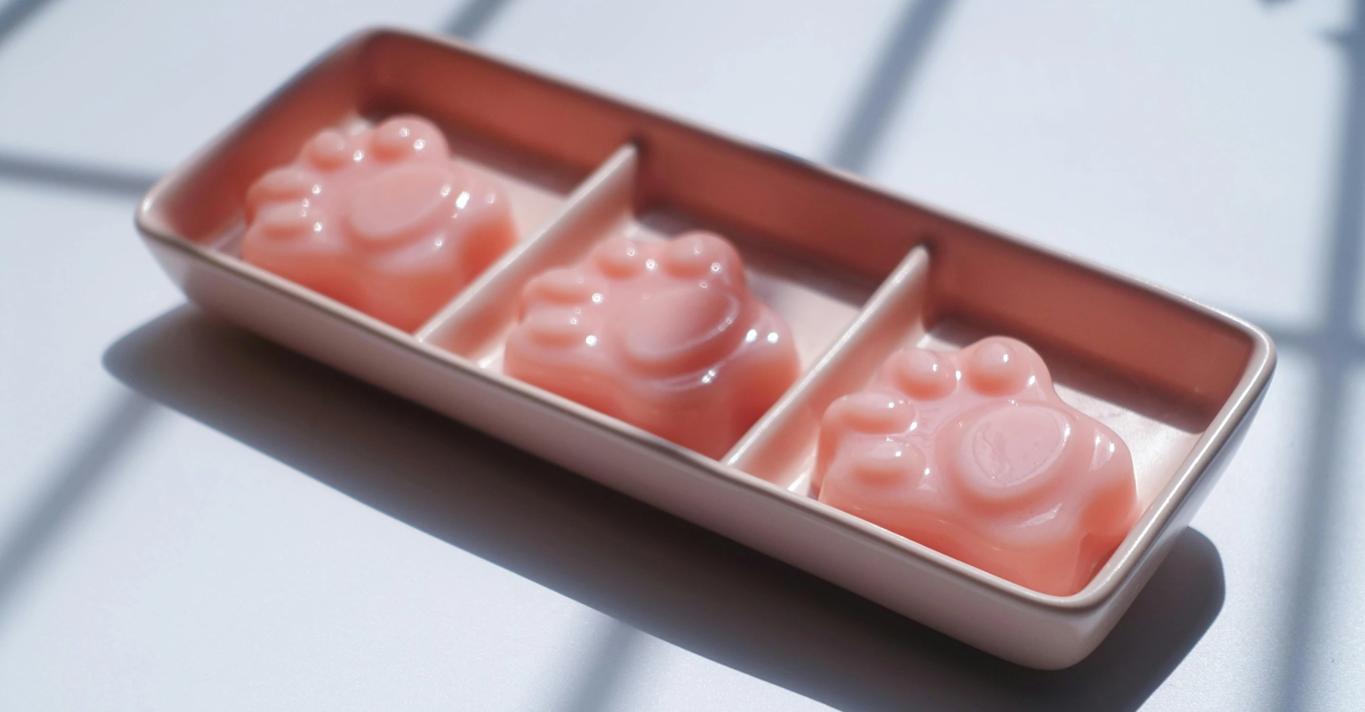 a container filled with pink soap sitting on top of a table, paw pads, threes, peach embellishment, koju morimoto