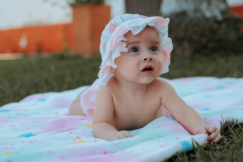 a baby laying on a blanket in the grass, pexels contest winner, wearing a white bathing cap, gif, pink, very beautiful girl