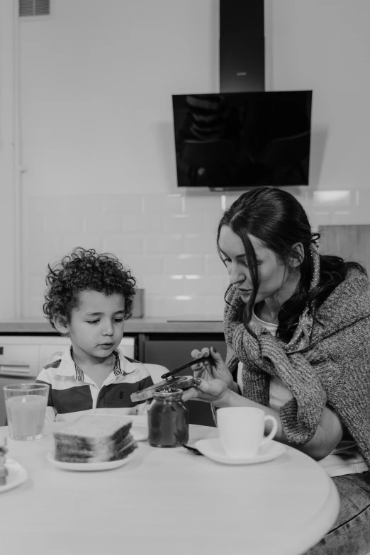 a woman sitting at a table with a child, a black and white photo, by Felix-Kelly, pexels, breakfast, cast, devon cady-lee, having a snack