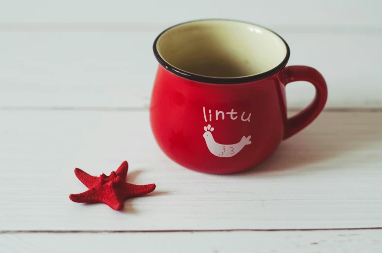 a red mug sitting on top of a wooden table, inspired by Lü Ji, starfish pose, with names, lina, bird