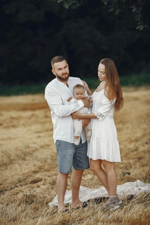 a man and woman holding a baby in a field, by Adam Marczyński, pexels contest winner, renaissance, handsome man, in white clothes, square, фото девушка курит