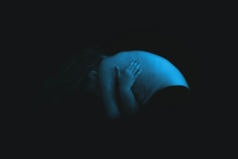 a woman in the dark covering her face with her hands, an album cover, inspired by Gottfried Helnwein, digital art, pregnant belly, neon blue, ffffound, from the side