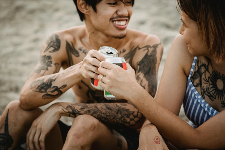 a man and a woman sitting next to each other on a beach, a tattoo, pexels contest winner, graffiti, holding a can of beer, manila, closeup of arms, fully body photo