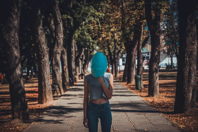 a woman walking down a sidewalk with a blue head covering her face, pexels contest winner, hair made of trees, sunfaded, a park, girls