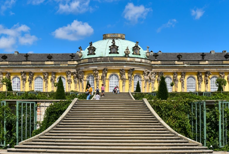 a group of people sitting on steps in front of a building, an album cover, by Thomas Häfner, pexels contest winner, rococo, royal garden landscape, yellow carpeted, palace on top of the hill, 17th-century