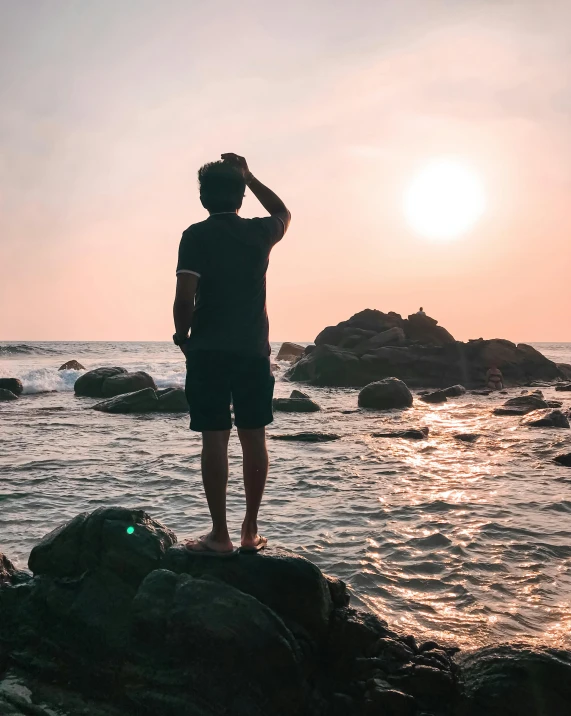 a man standing on top of a rock next to the ocean, profile image, sunset photo, beach pic, asian male