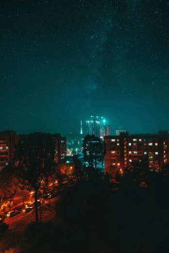 a view of a city at night from the top of a hill, by Adam Marczyński, soviet apartment buildings, teal sky, galaxy, low quality photo
