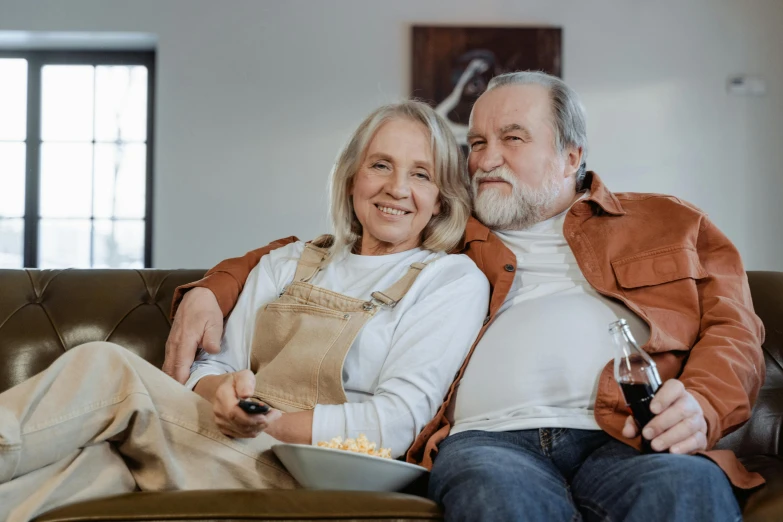 a man and woman sitting on a couch watching tv, a portrait, pexels, renaissance, overalls and a white beard, middle aged, brown, promotional image