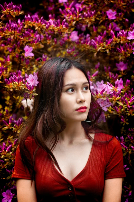 a woman standing in front of a bush of flowers, inspired by Ruth Jên, pexels contest winner, beautiful young asian woman, red and purple, 7 0 mm photo, 5 0 0 px models