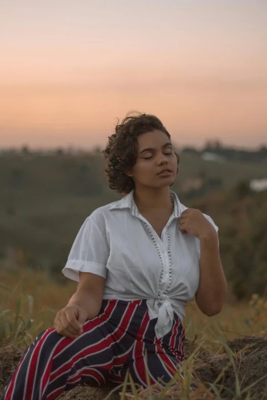 a woman sitting on top of a pile of hay, an album cover, trending on unsplash, renaissance, wearing a white button up shirt, ((sunset)), mixed-race woman, distant thoughtful look