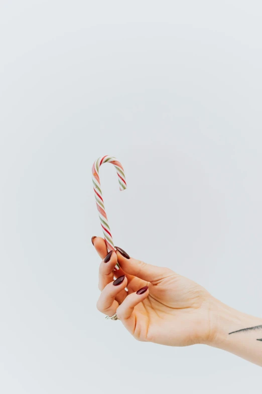 a person holding a candy cane in their hand, a colorized photo, pexels, minimalism, lightroom preset, unsplash transparent, made of glazed, tall