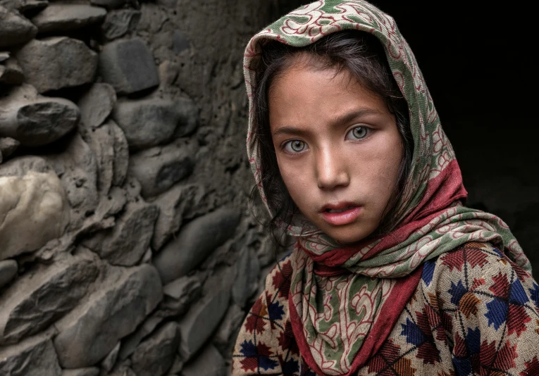 a young girl standing in front of a stone wall, a portrait, inspired by Steve McCurry, unsplash contest winner, the eyes of sharbat gula, in a village, 8k resolution”, award - winning photo. ”