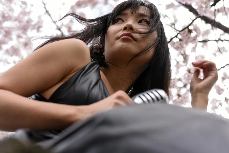 a woman in a black dress sitting under a tree, an album cover, unsplash, wearing atsuko kudo latex outfit, sydney park, cherry blossoms in the wind, wearing a full leather outfit