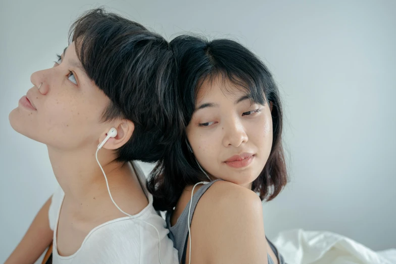 a couple of women sitting on top of a bed, by Jang Seung-eop, trending on pexels, earbuds, sideburns, over his shoulder, facing each other