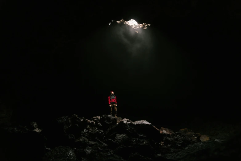 a person standing on a rock in the dark, looking at the ceiling, crater, bjørn skalldrasson, single light