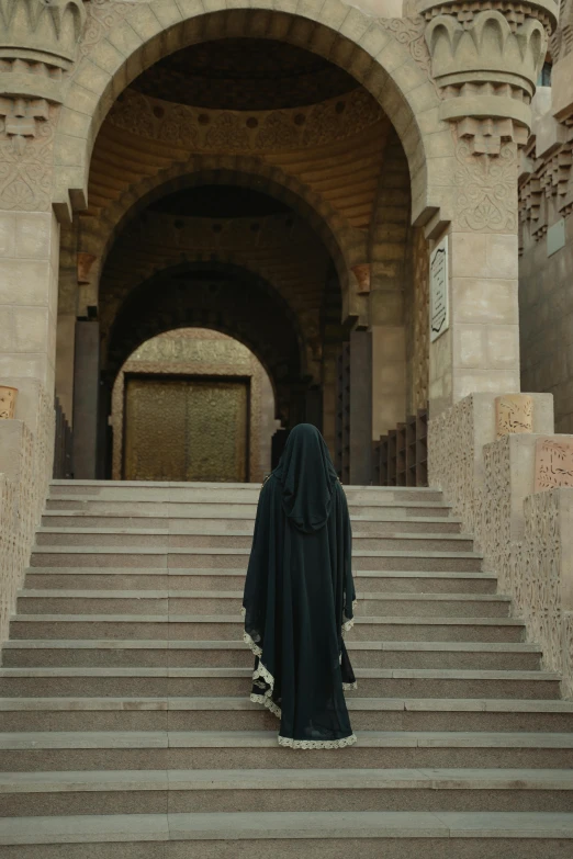 a woman in a black robe standing in front of a building, inspired by Osman Hamdi Bey, pexels contest winner, symbolism, obscured hooded person walking, egypt, ( ( theatrical ) ), monastery