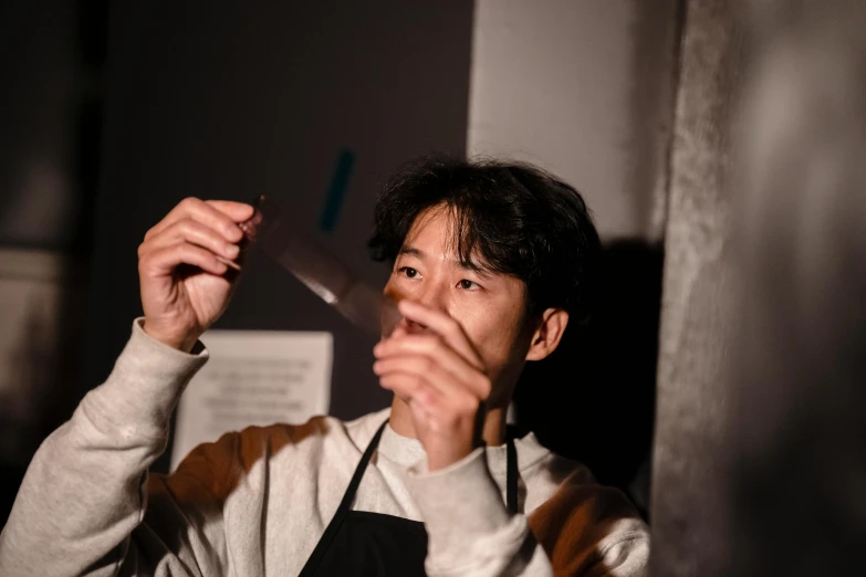 a man holding a knife in front of his face, a picture, unsplash, shin hanga, mixing drinks, looking partly to the left, partially cupping her hands, closed limbo room