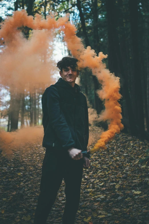 a man standing in the woods holding an orange smoke bomb, a picture, declan mckenna, profile image, color picture, headshot profile picture