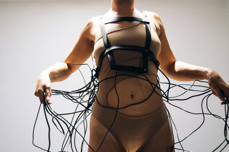 a woman holding a bunch of wires in her hands, an album cover, inspired by Hans Bellmer, unsplash, interactive art, body harness, inflatable, huge belt, lachlan bailey