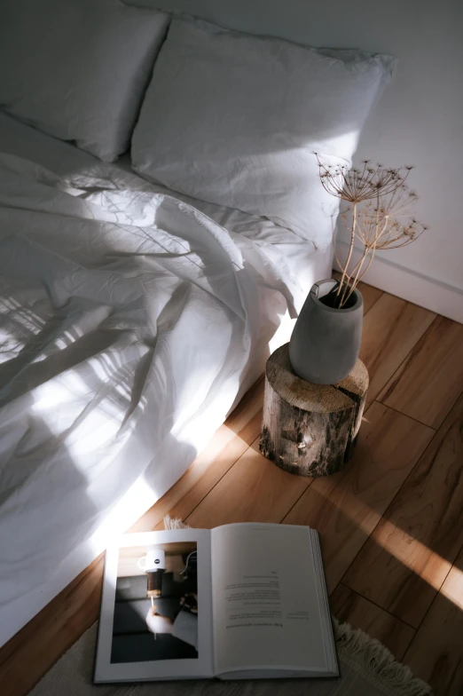 a book sitting on top of a wooden floor next to a bed, unsplash contest winner, light and space, white vase, sunflare, jinyoung shin, wood accents