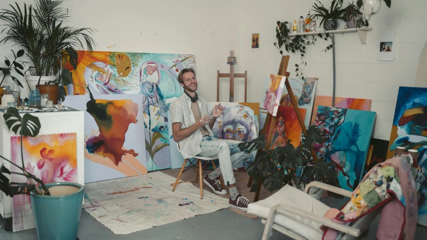 a man sitting in a chair in front of a painting, inspired by James Jean, pexels contest winner, in a white boho style studio, melinda matyas, peter mohrbacher and takayuk, mate painting